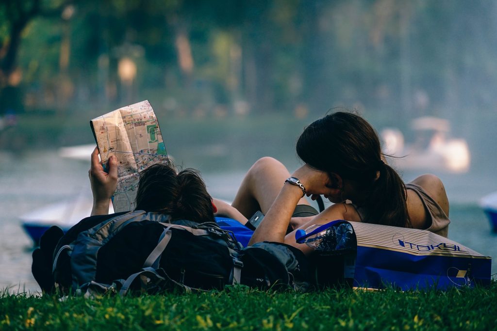 Two people sitting on the grass reading a newspaper.