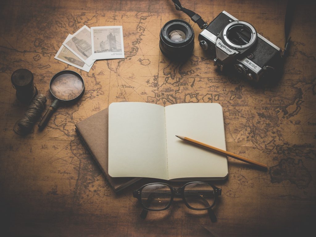A notebook, magnifying glass, camera and other explorer's items laid out on a flat surface.