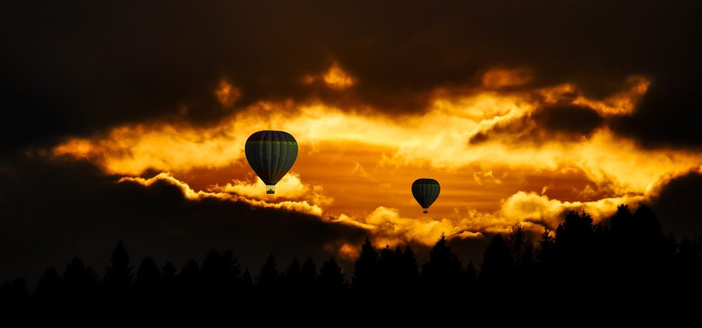 Two hot air balloons floating over a scenic landscape at sunrise.