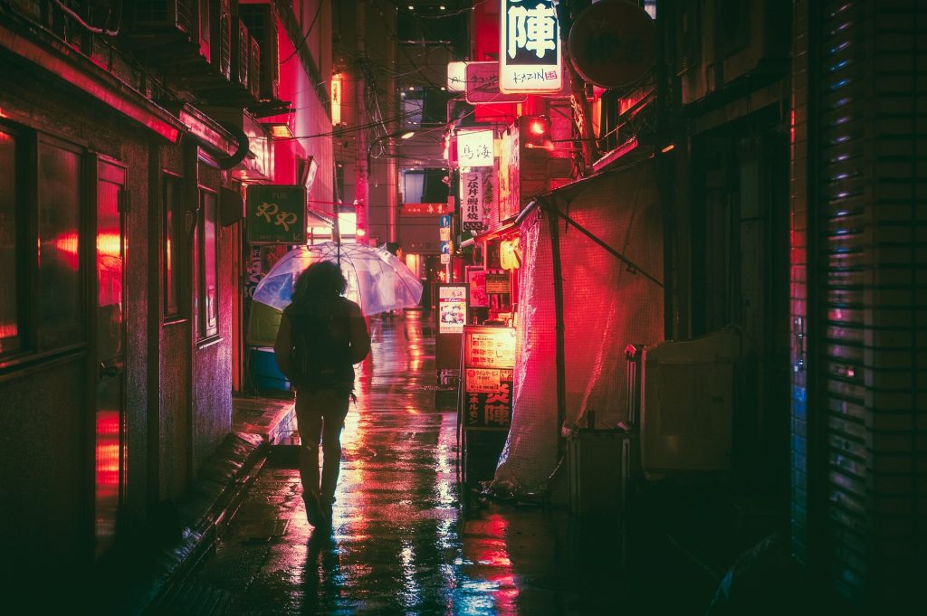 A narrow pedestrian street at night, a single person walking sillhouetted against a pink neon glow.