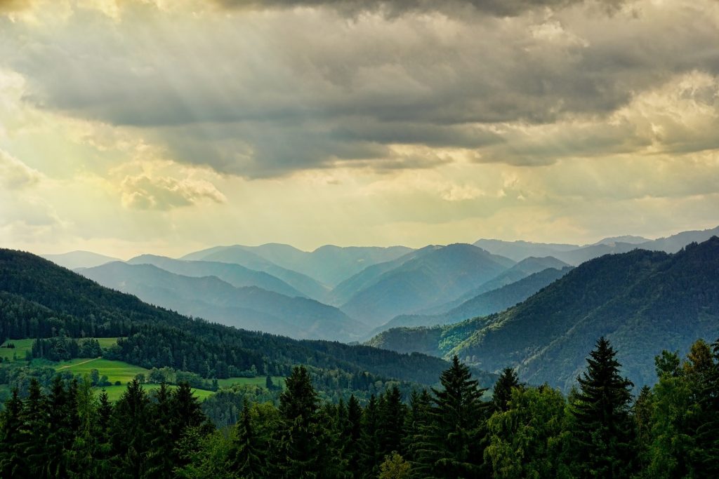 A cloudy sky over a valley with trees and mountains.
