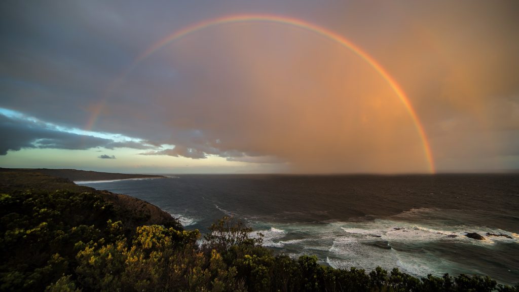 A rainbow is seen over the ocean and cliffs.