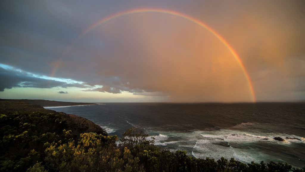 A rainbow arching over a lush green landscape and a lake.