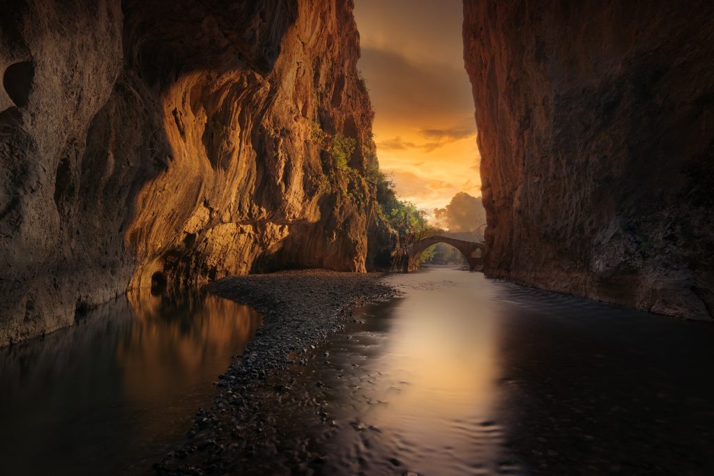 A calm waterway with tall mountains on either side, sunset off in the distance.
