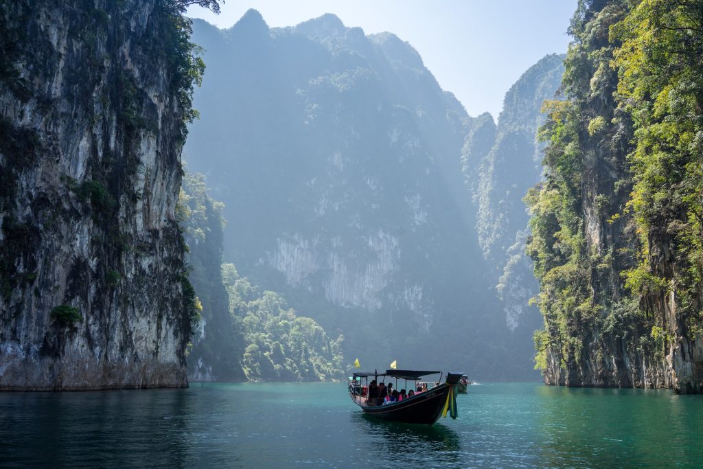 A calm waterway with tall mountains on either side, a boat sailing between them.