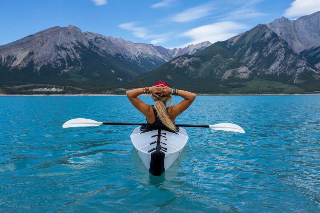 A woman is paddling a kayak in a lake with mountains in the background.