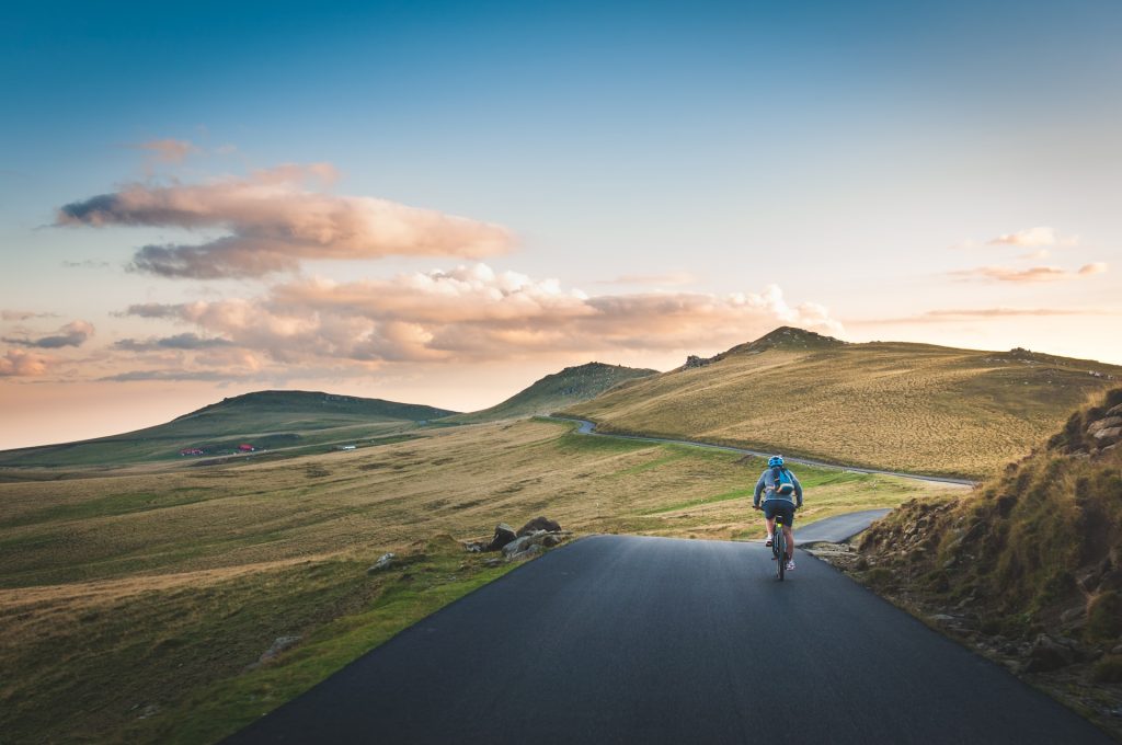 A small road or bicycle pathway on grassy hilly terrain, a cyclist on the road.