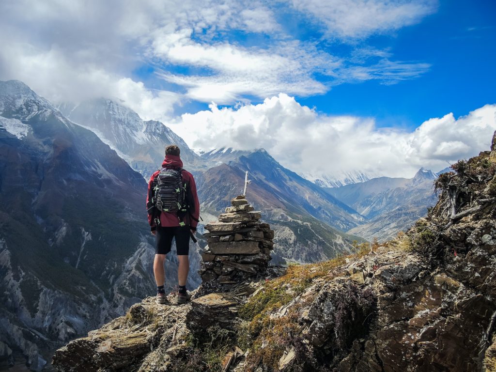 A hiker in a mountain range, looking out at the peaks stretching beneath a bright blue sky.