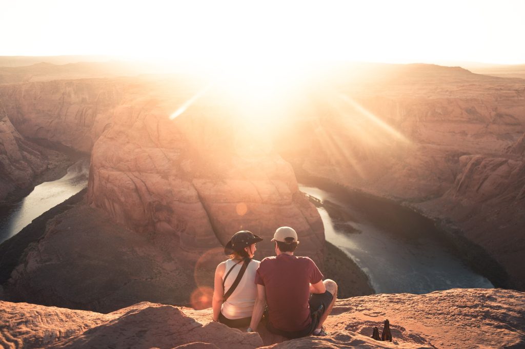 Two people sitting on a cliff overlooking a canyon at sunset.