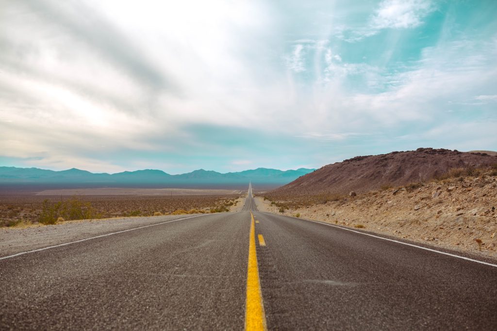 An empty road in the desert with mountains in the background.