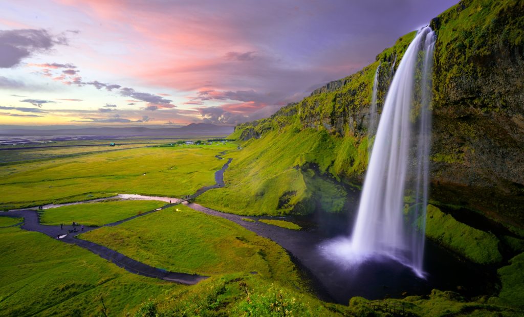 Water falling from a high, grassy clifftop onto the grassland below.