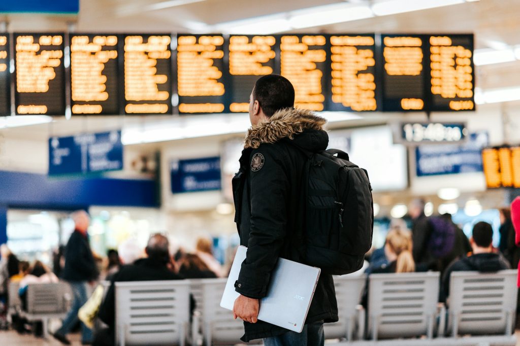 A man in an airport / train station looks up at the information screens.