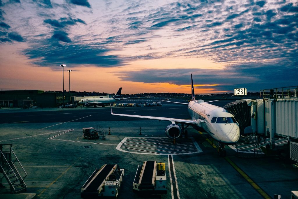 A plane is docked at an airport gate during a vibrant sunset on a cloudy day.