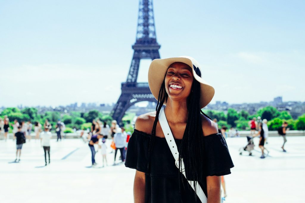 A woman smiling as she stands in front of the Eiffel Tower in Paris.