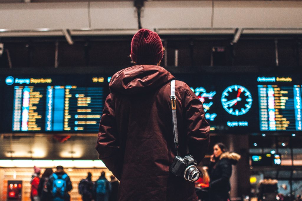 A traveller seen from behind, looking at the information boards at a railway station or airport.