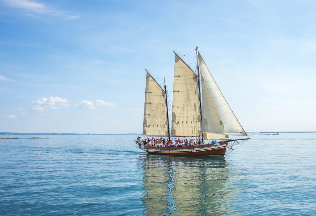 Elegant sailing ship with three large sails gliding on calm, clear waters under a bright blue sky.