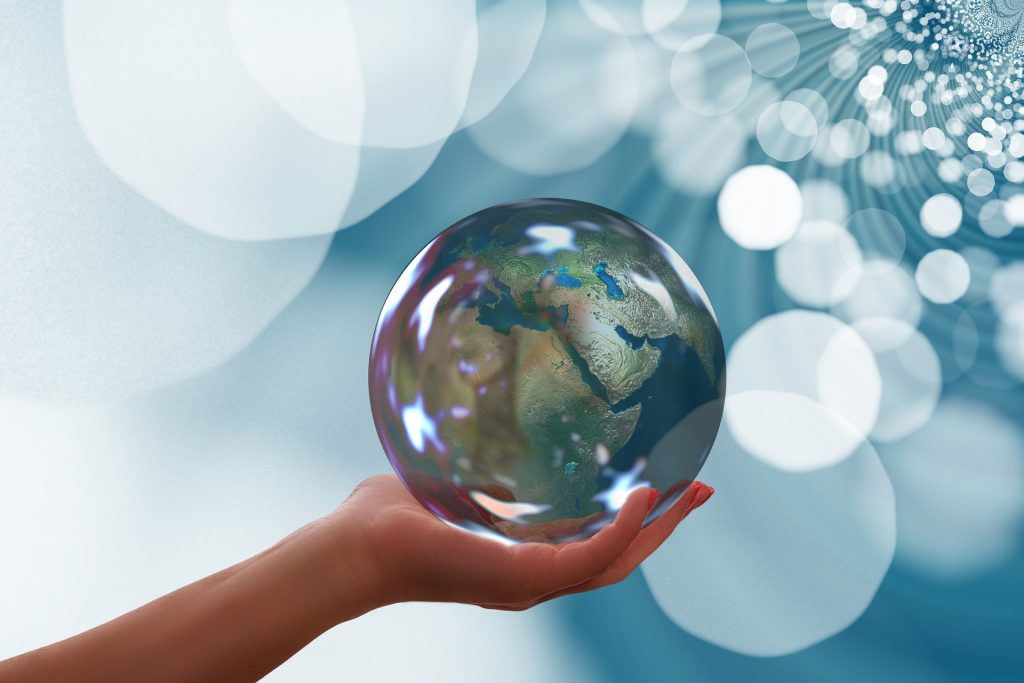 Hand holding a transparent globe with Earth inside, set against a dreamy background of bokeh lights and abstract patterns.
