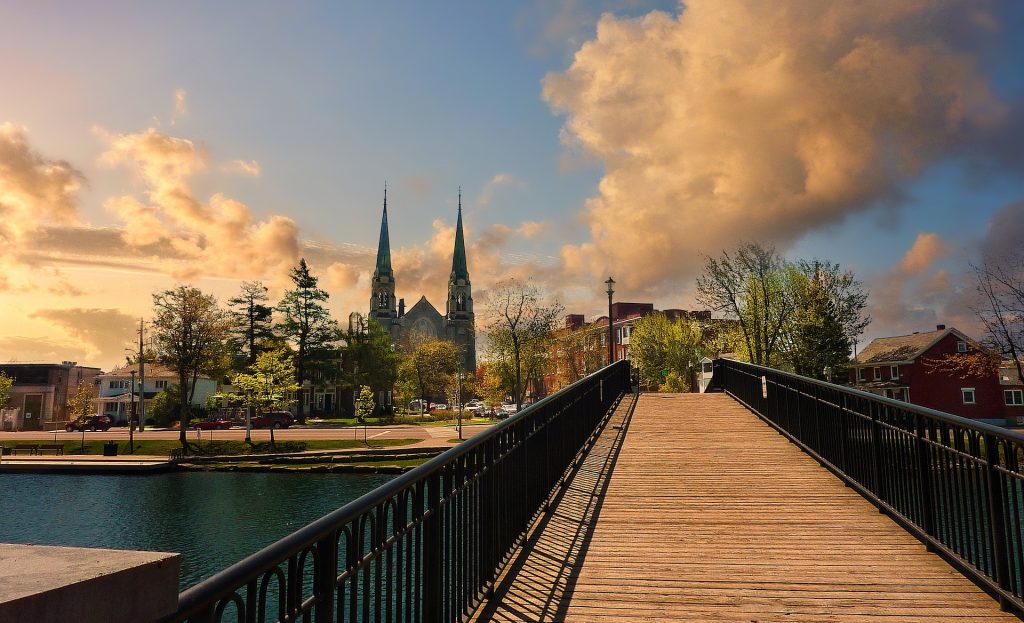 Wooden bridge leading toward a historic church in Ottowa, framed by trees and a vibrant sky with dramatic clouds at sunset.