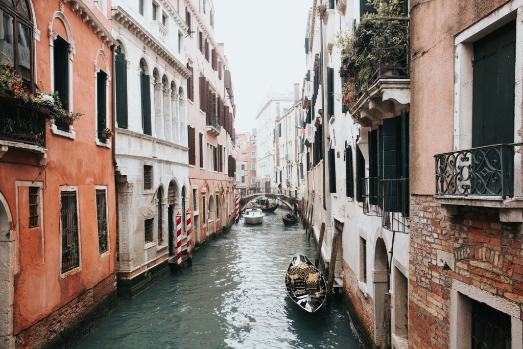 A peaceful Venice canal with colorful historic buildings, a gondola, and blooming flowers on balconies.