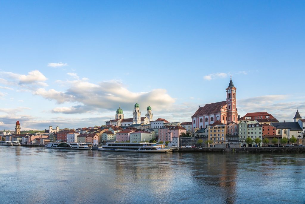 Scenic view of Passau, Germany, with colorful buildings, historic churches, and the Danube River under a clear sky.
