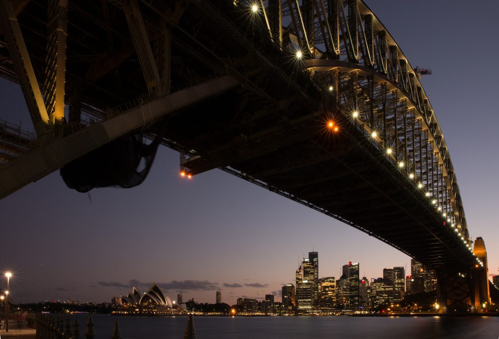 Iconic Sydney Harbour Bridge at night with the Opera House and city skyline illuminated in the background.