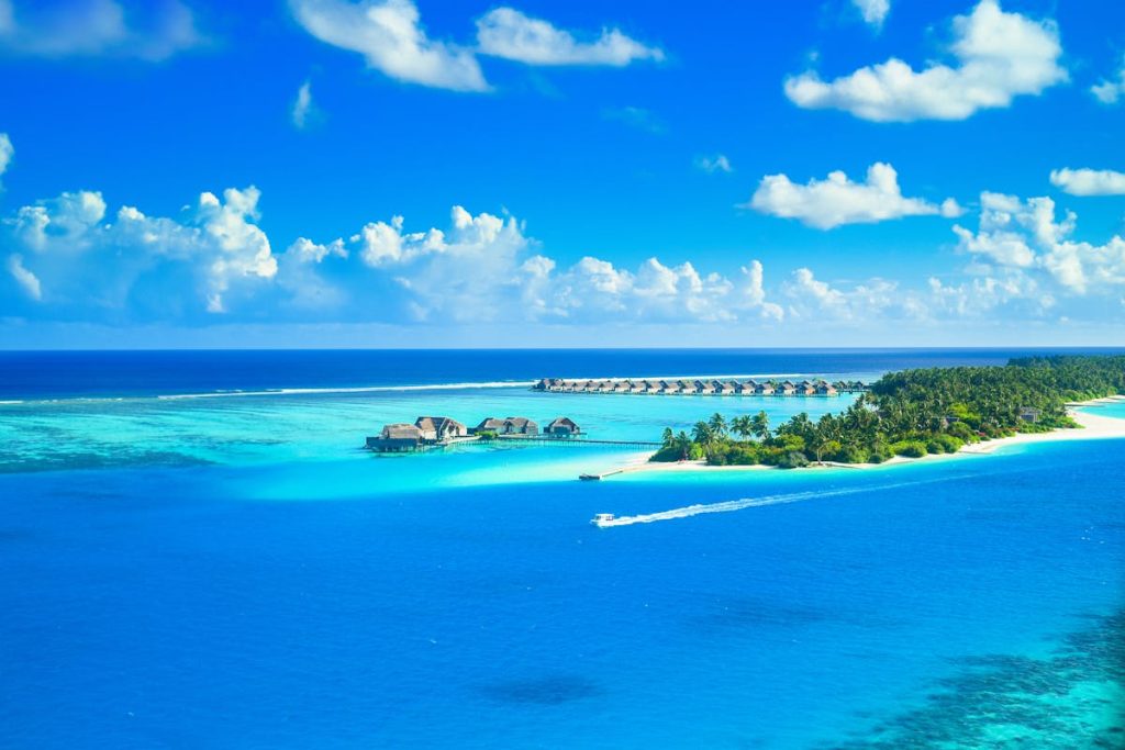 Tropical island with turquoise waters, lush greenery, overwater bungalows, and a small boat under a blue sky.