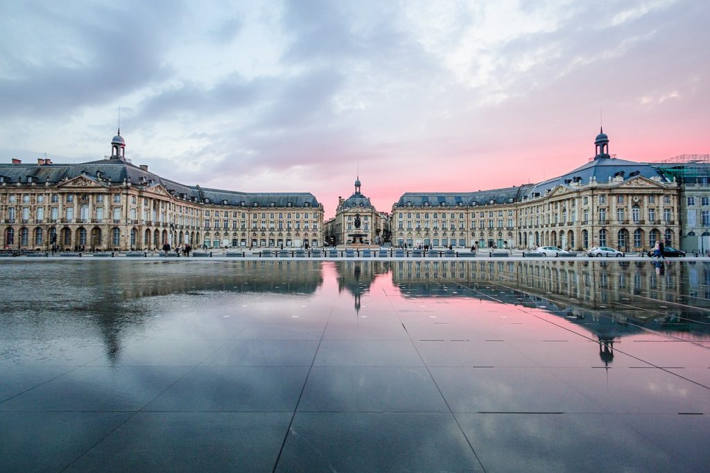 Historic buildings reflected in calm water at dawn, with soft pink and blue skies enhancing the peaceful scene.